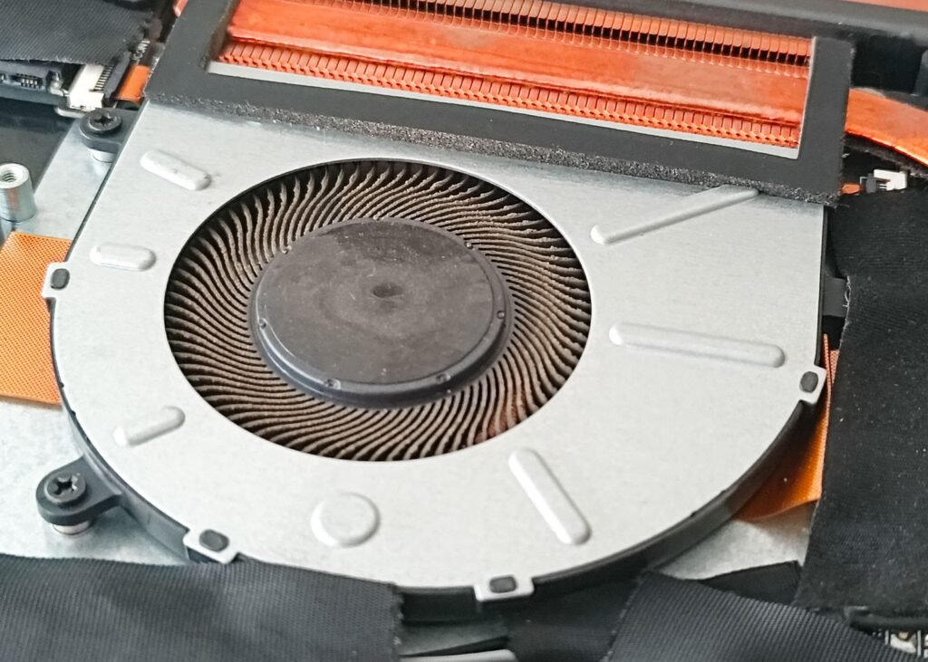 Close-up of a dusty internal cooling fan and copper heat pipes exposed inside a laptop chassis.